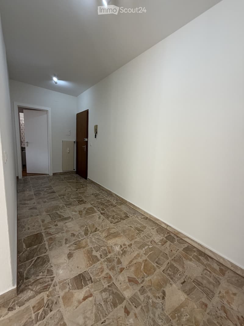 Empty hallway with stone tiled floor, white walls, and two doors leading to other rooms.