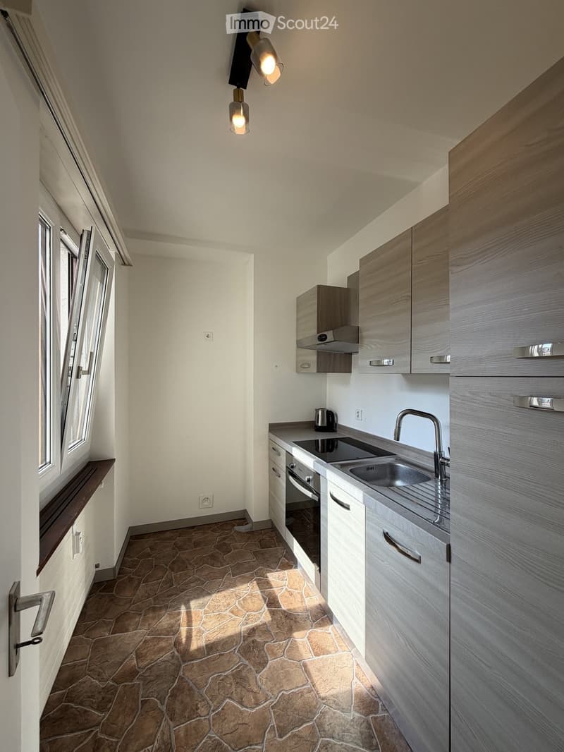 Modern kitchen with grey cabinets, stone tiled floor, stainless steel sink, and a coffee maker on the counter.