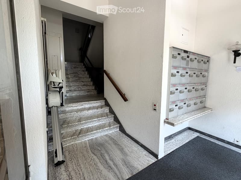 Hallway with marble flooring, staircase leading upwards, mailboxes on the right, and a mobility aid device on the left.