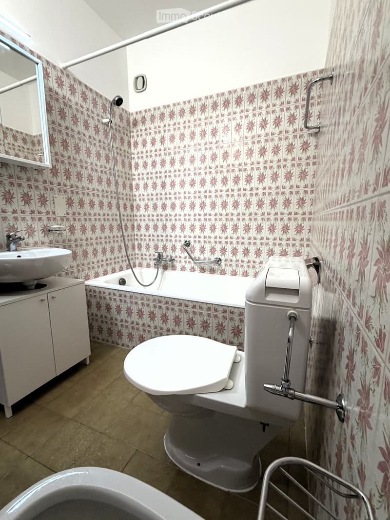 Bathroom with floral patterned tiles, a sink, bathtub, toilet, and a mirror above the sink.