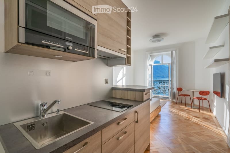 Modern kitchen with wooden cabinets, stainless steel sink, microwave, induction cooktop, and a small dining area with a table and chairs.
