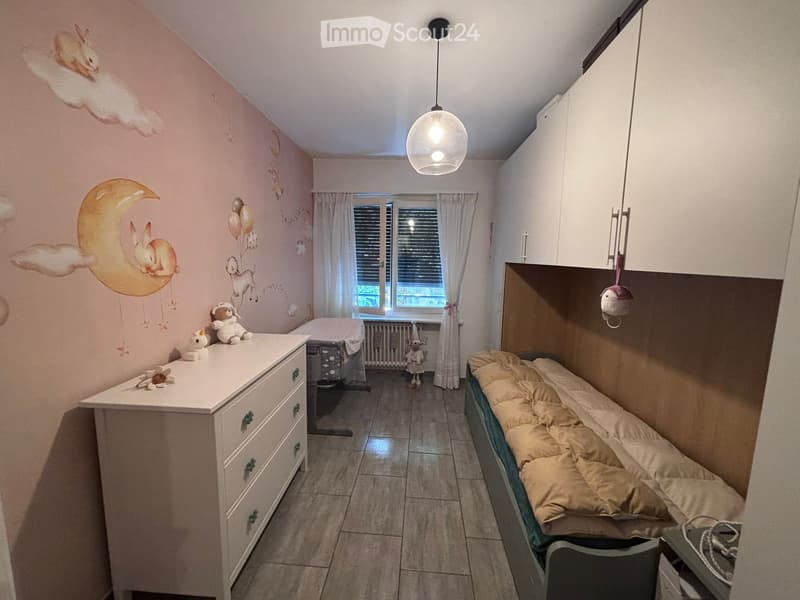Cozy children's bedroom with a single bed, dresser, and decorative wall art featuring animals and celestial themes. Includes a small play area with toys and a hanging toy.
