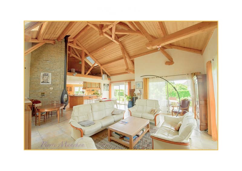Open-plan living and dining area with exposed wooden beams, a white leather sofa, coffee table, dining table, and a modern fireplace.