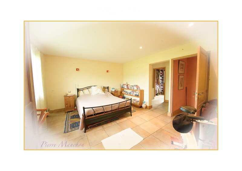 Bright bedroom with a metal-framed bed, nightstands, bookshelf, and an open closet. The room features tiled flooring and warm lighting.