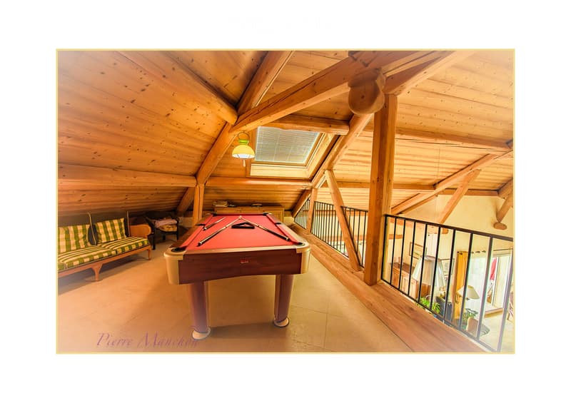 Cozy attic room with wooden beams, skylight, sofa, pool table, and a view of the lower level through a railing.