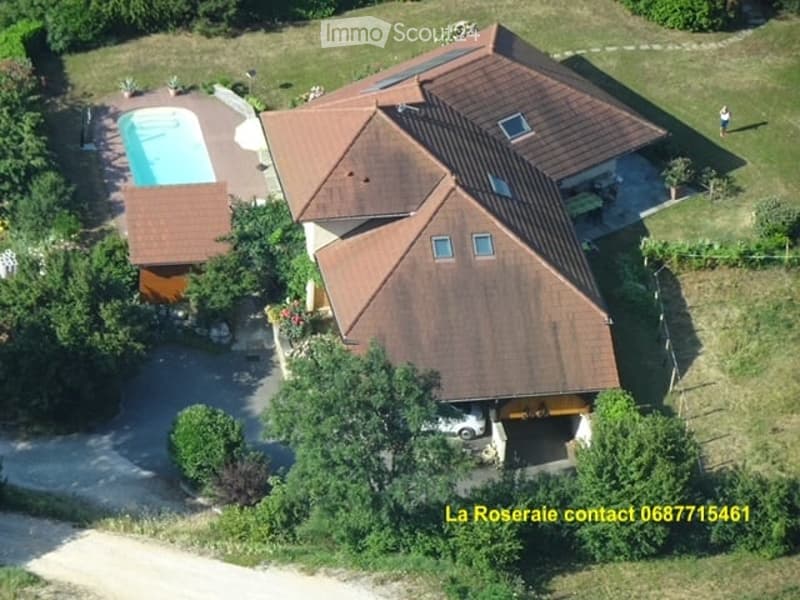 Aerial view of a two-story house with a brown tiled roof, surrounded by greenery, featuring a swimming pool, garage, and parking area.