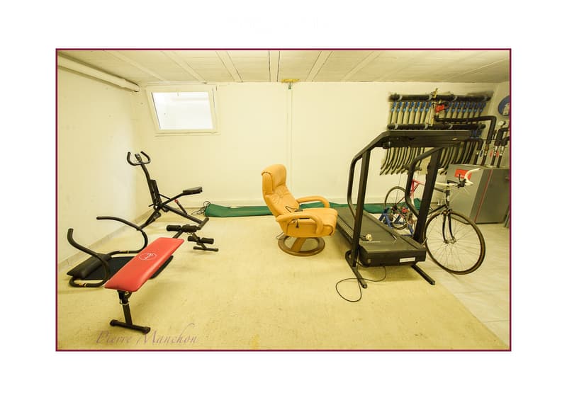 Well-lit room with exercise equipment including an elliptical machine, a bench, a chair, a bicycle, and a treadmill, along with various pipes and storage units.