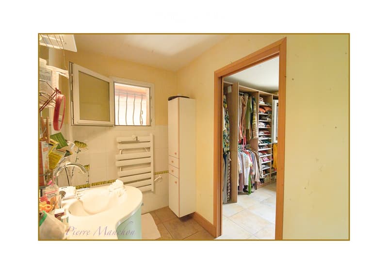 Bathroom with a sink, faucet, mirror, radiator, and a closet with clothes and shelves visible through an open door.