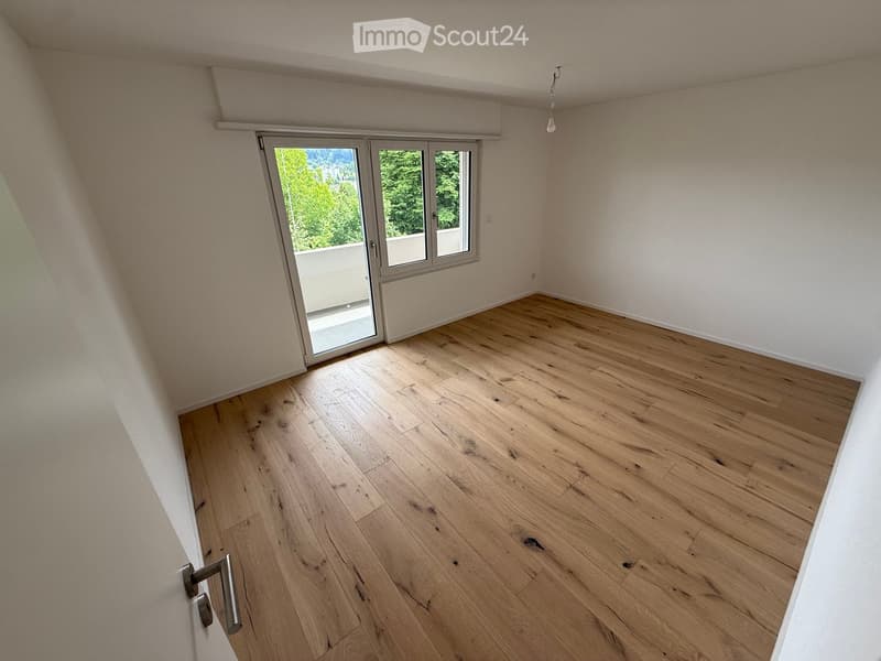 Empty room with wooden flooring, white walls, and a large sliding glass door leading to a balcony.