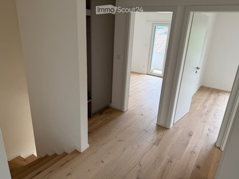 Empty hallway with light wooden flooring, white walls, and open doors leading to other rooms.