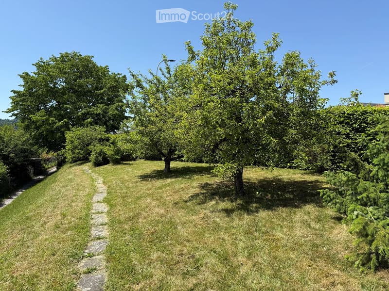 A well-maintained garden with a stone pathway, lush green grass, and several trees providing shade.