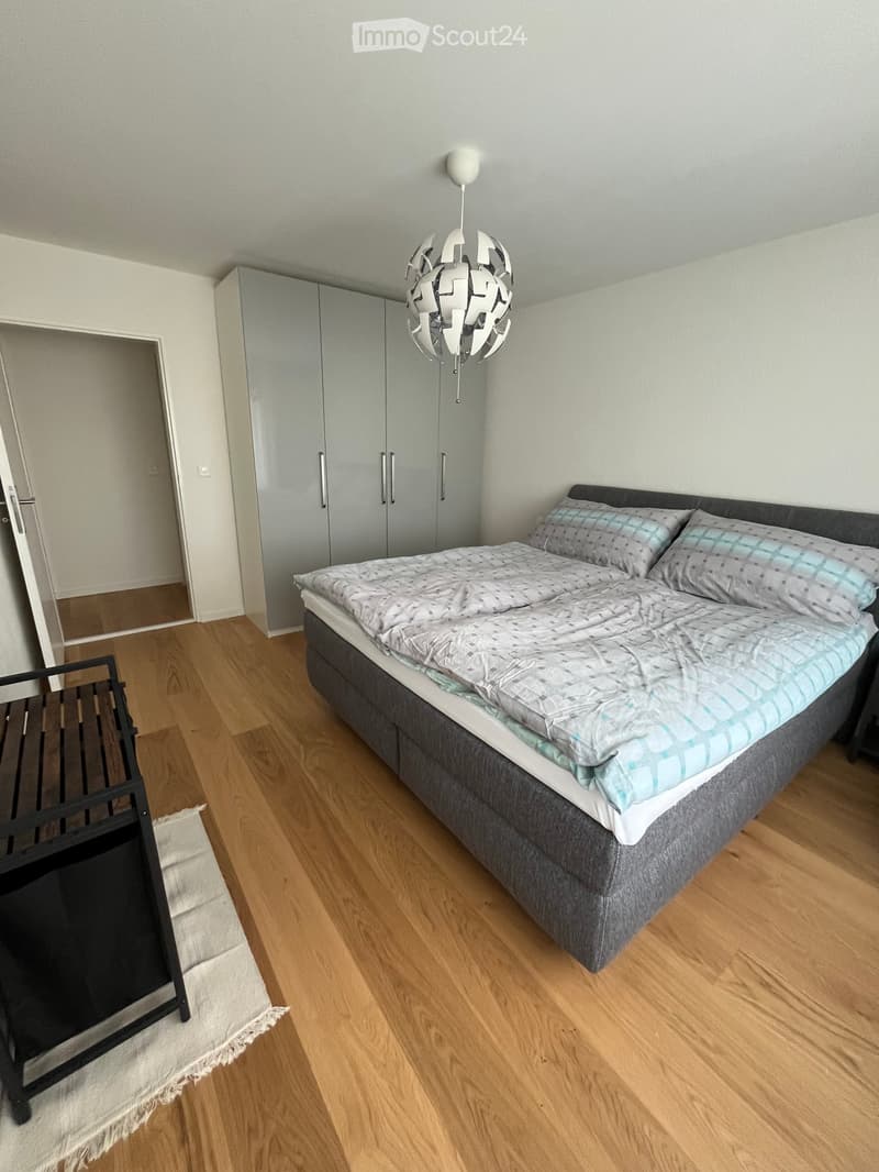 Modern bedroom with a double bed, grey bedding, a wardrobe, a chair, and a decorative lamp.