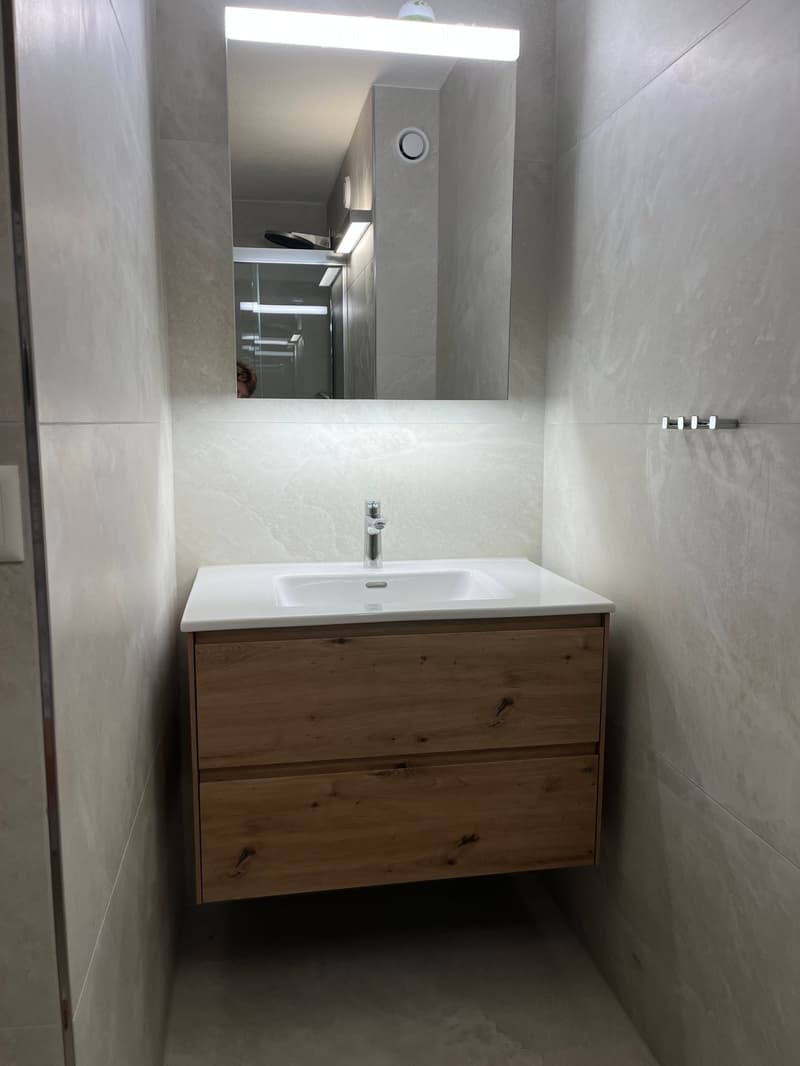 Modern bathroom with a white sink, wooden cabinet, and large mirror with built-in lighting.