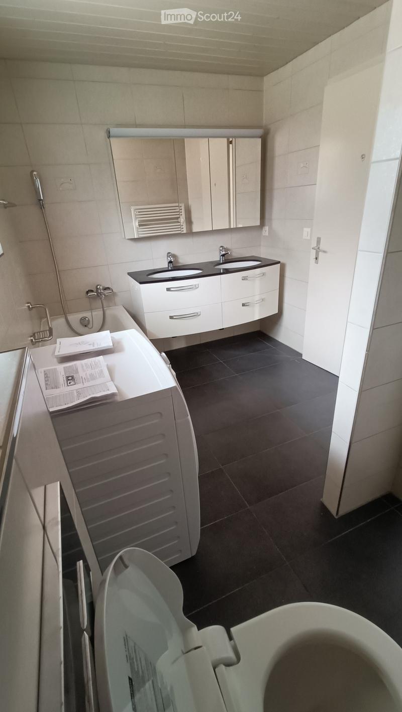 Modern bathroom with a double sink, mirror, bathtub, and radiator. The space features white cabinets, black countertops, and dark tiled flooring.