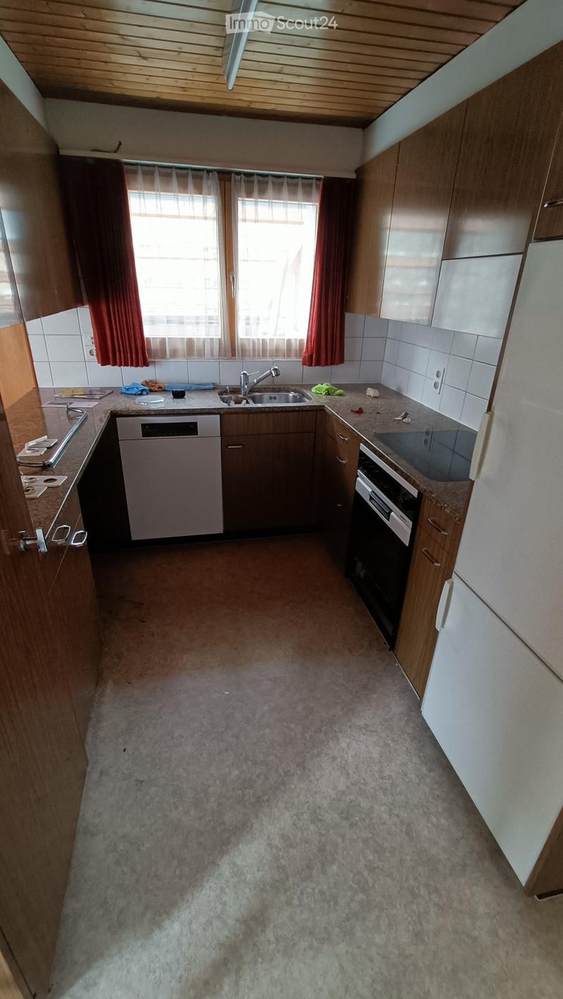 Modern kitchen with wooden cabinets, stainless steel appliances, and a tiled backsplash. The space includes a sink, dishwasher, and oven, with a window and red curtains providing natural light.