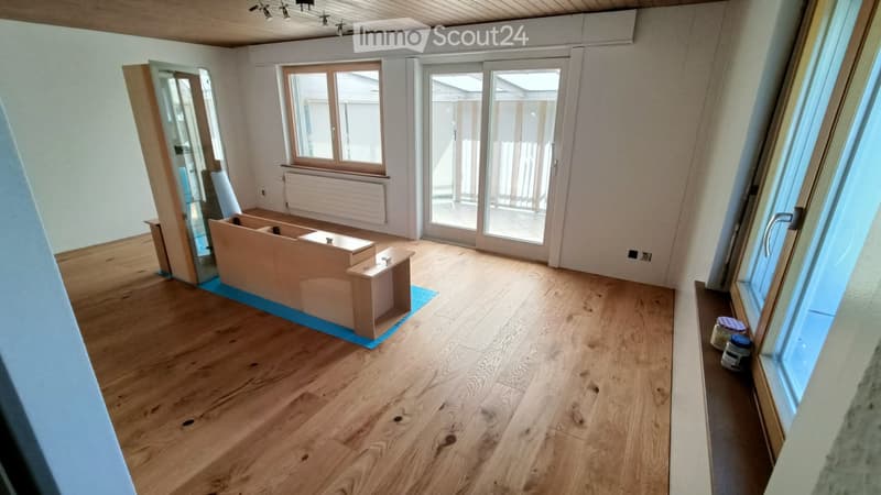 Empty room with wooden flooring, large windows, and a sliding glass door leading to a balcony. The room is unfurnished with only a few construction materials and tools visible.