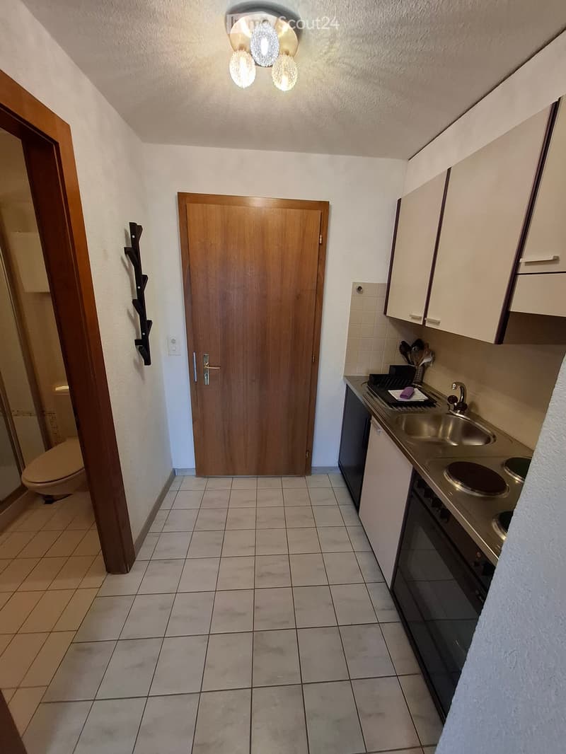 A small kitchen area with a sink, faucet, oven, and cabinets, connected to a bathroom with a toilet.