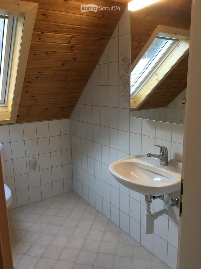 bathroom with tiled floors, white sink, mirror, toilet, sloped wooden ceiling, window