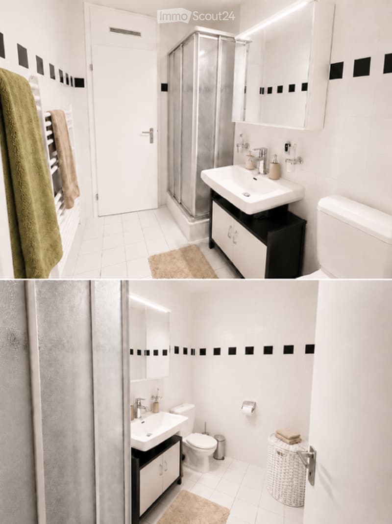 Modern bathroom with white tiles, black accent border, sink with mirror, toilet, shower, and wicker basket on floor.