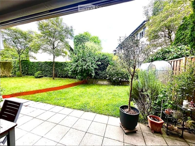 Well-maintained garden with a lawn, trees, and potted plants on a tiled patio area.