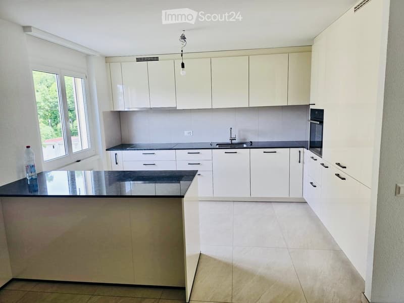 Modern kitchen with white cabinets, black countertops, and a central island. Features a sink, oven, and a bottle on the counter.