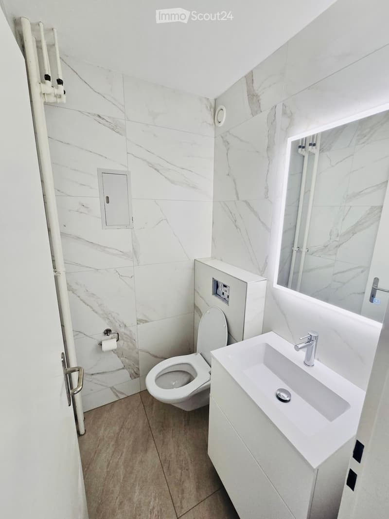 Modern bathroom with white marble tiles, a toilet, a sink with a modern faucet, and a mirror above the sink.