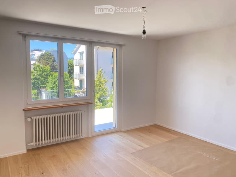 Empty room with light wooden flooring, white walls, large windows, and a radiator. No furniture or equipment present.
