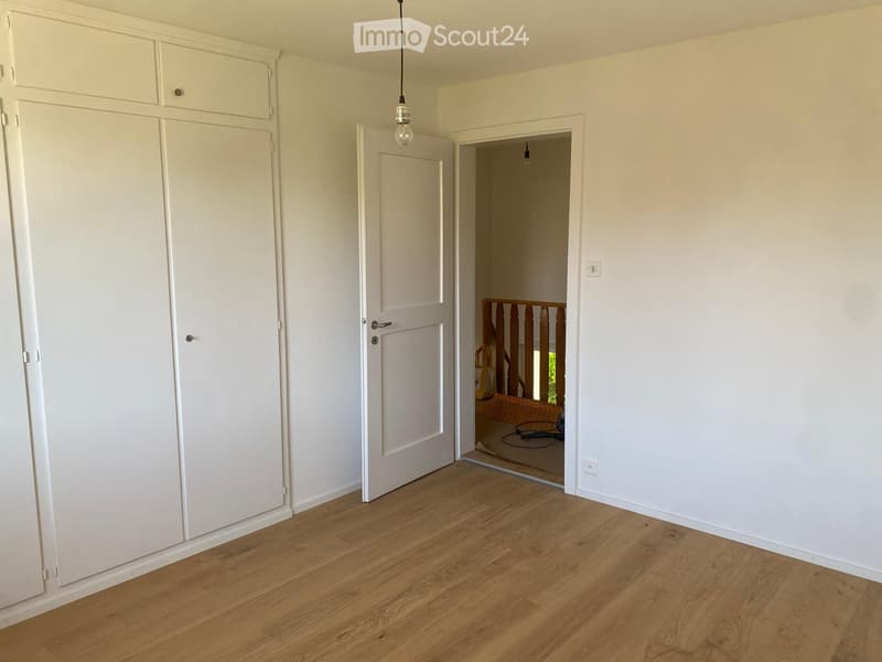 Empty room with light wooden flooring, white walls, built-in white wardrobes, and a doorway leading to another room with a visible staircase.