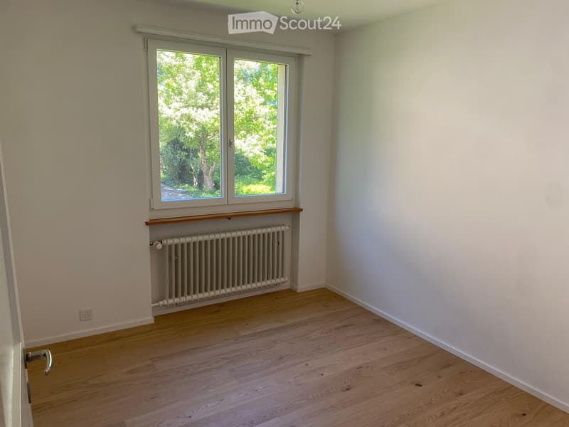 Empty room with light wooden flooring, white walls, and a window with a radiator below it.