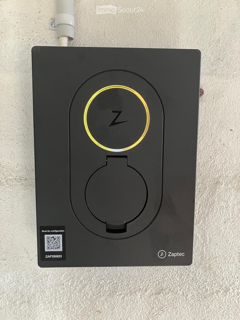 A black wall-mounted charging station with a circular charging pad and a QR code for configuration.