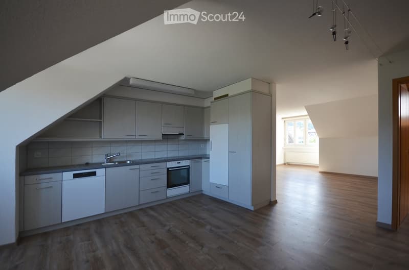 Modern kitchen with grey cabinets, stainless steel appliances, and wooden flooring. Adjacent unfurnished room with large window and wooden floor.