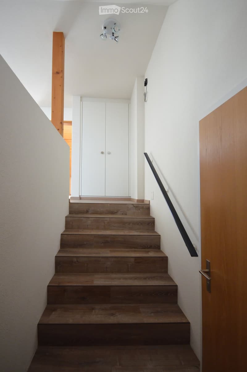 Wooden staircase with a modern black railing, white walls, and a ceiling light fixture.