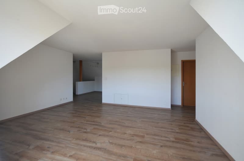 Empty room with wooden flooring and white walls, featuring a doorway and visible electrical outlets.