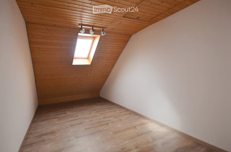 Empty attic space with wooden walls, ceiling, and floor, featuring a skylight window and recessed lighting fixtures.
