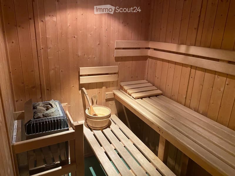 Wooden sauna interior with benches, a stone stove, a wooden bucket, and a wooden paddle.