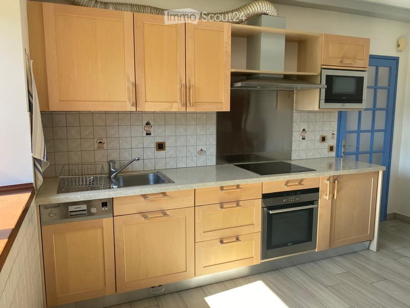 Modern kitchen with light wooden cabinets, stainless steel appliances, and a tiled backsplash.