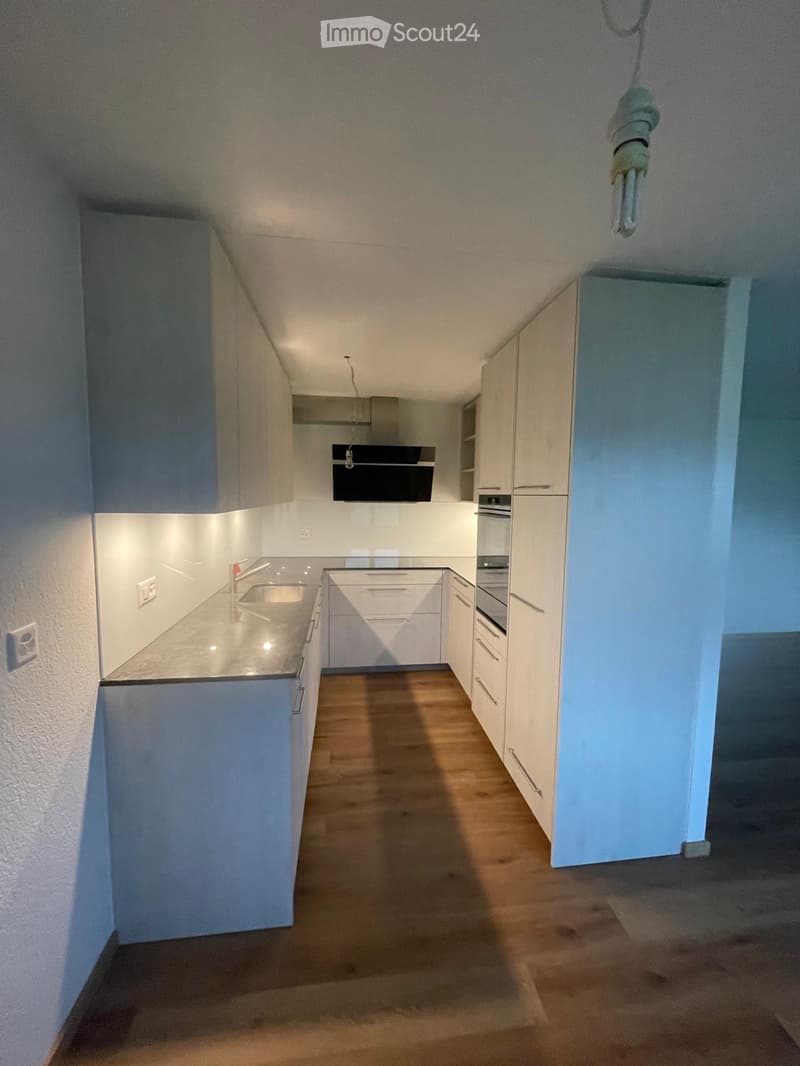 Modern kitchen with white cabinets, wooden floor, sink, and oven. Minimalist design with clean lines and bright lighting.
