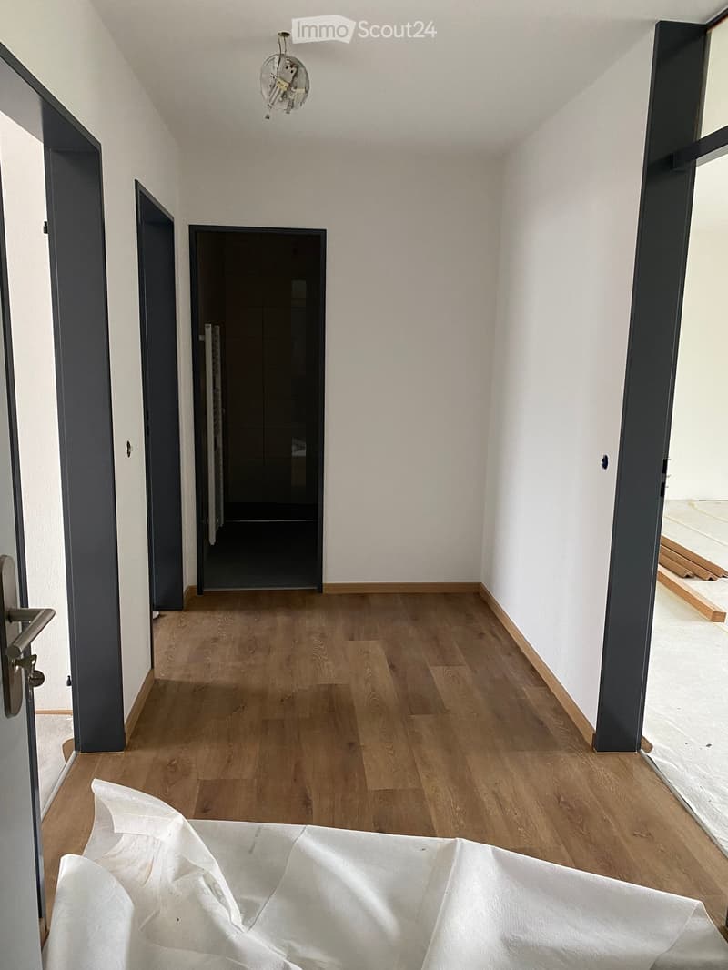 Empty hallway with wooden flooring, white walls, and several doors leading to other rooms. A light fixture is visible on the ceiling.
