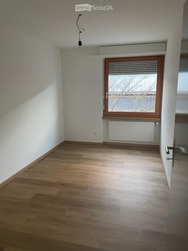 Empty room with light wooden flooring, white walls, and a window with a radiator below it.