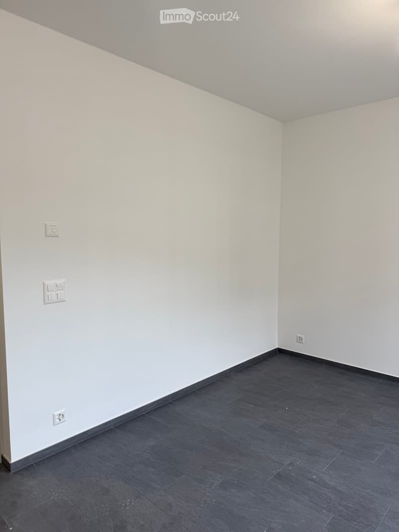 Empty room with white walls and dark grey tiled floor, featuring electrical outlets on the walls.
