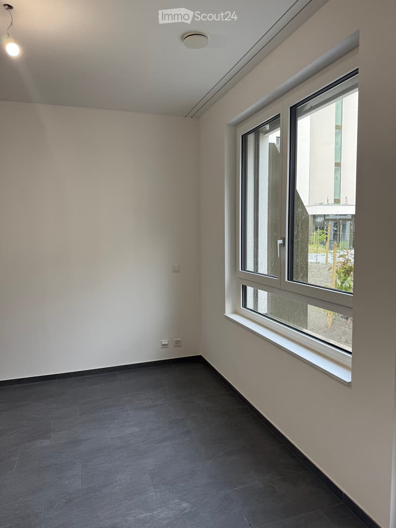 Empty room with dark tiled floor, light-colored walls, and large windows with blinds. No furniture or equipment visible.