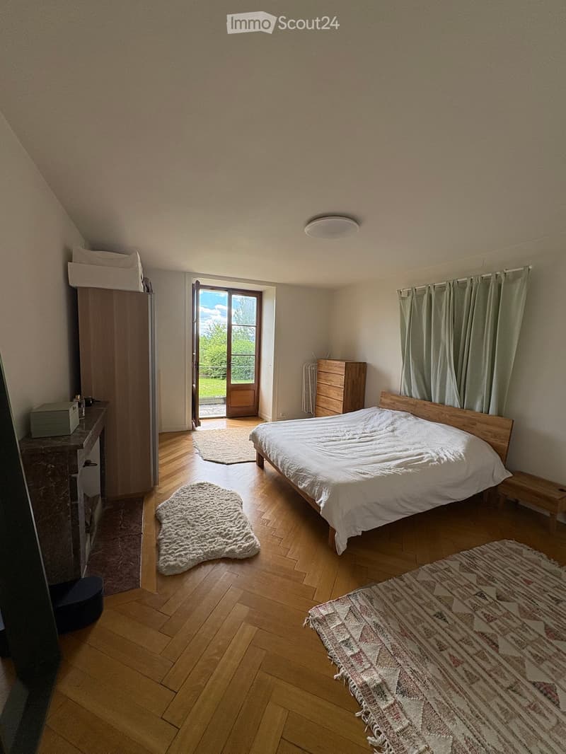 Cozy bedroom with wooden flooring, a bed with white bedding, a wardrobe, a nightstand, and rugs.