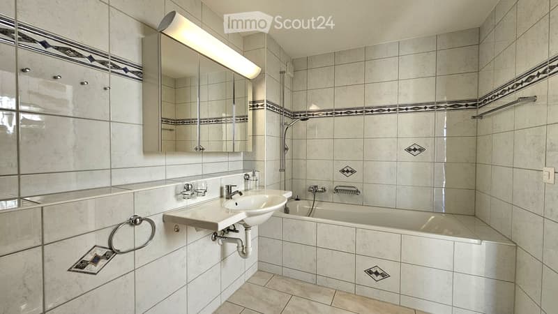 Modern bathroom with white tiles, a sink, bathtub, mirror, and towel rack.