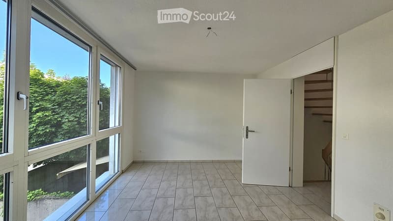 Empty room with large windows, tiled floor, and a door leading to a staircase.