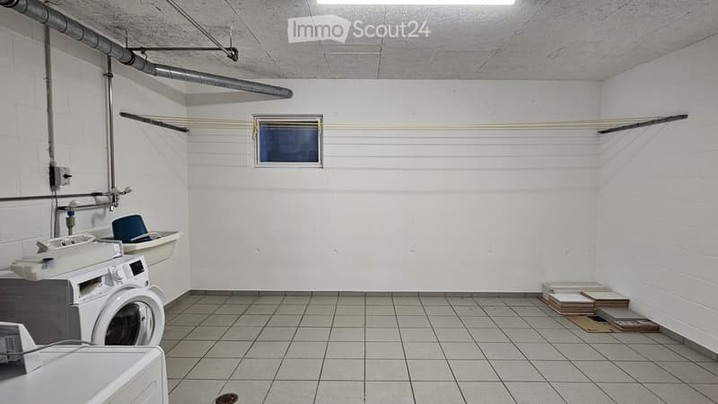 Utility room with white tiled floor, white brick walls, washing machine, dryer, sink, and a small stool.