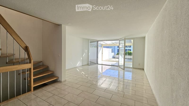Bright hallway with tiled floor, wooden staircase, and large glass doors leading to an outdoor area.