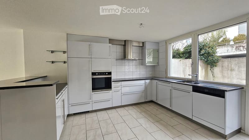 Modern kitchen with white cabinets, stainless steel appliances, and a large window overlooking a garden.