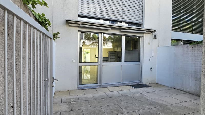 Modern building entrance with glass doors, metal gate, and tiled pavement.