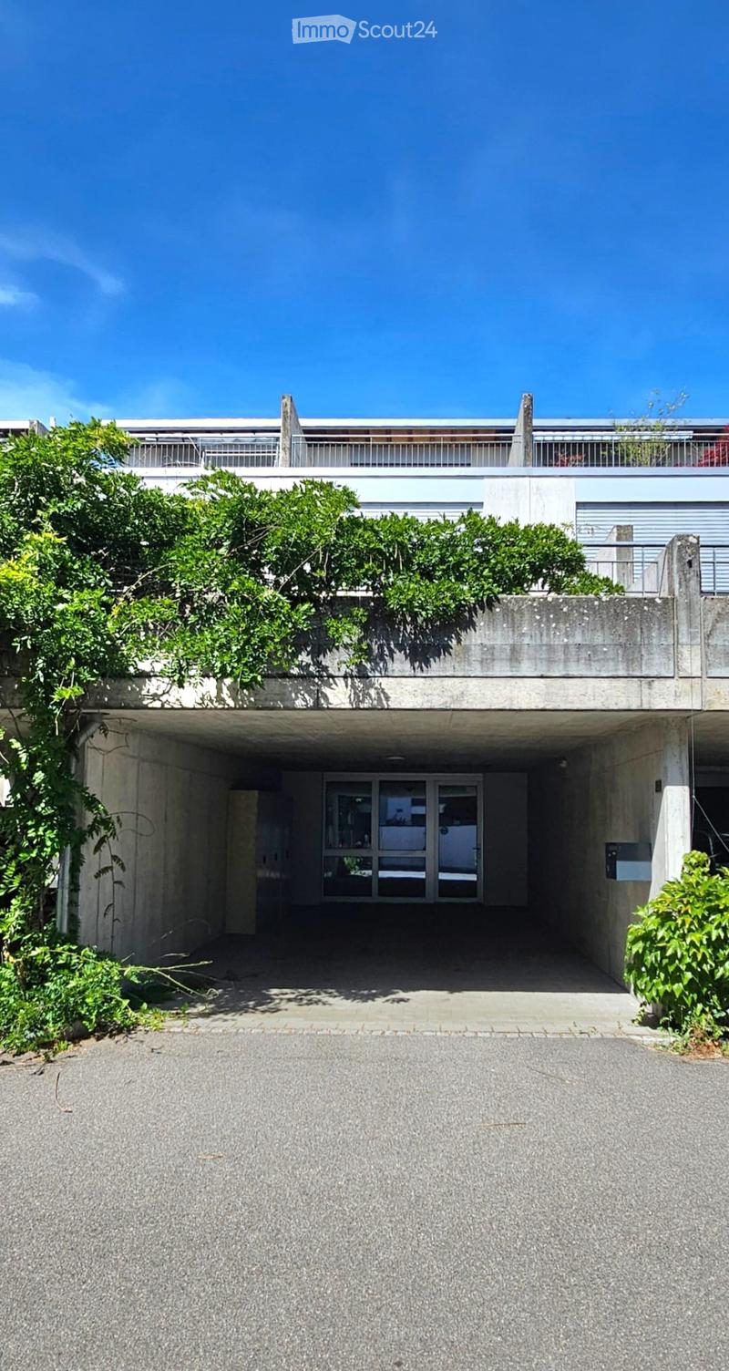 Modern concrete building with a covered entrance, greenery on the roof, and a spacious driveway.