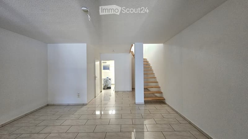 Empty hallway with tiled floor, white walls, and a wooden staircase leading upwards.
